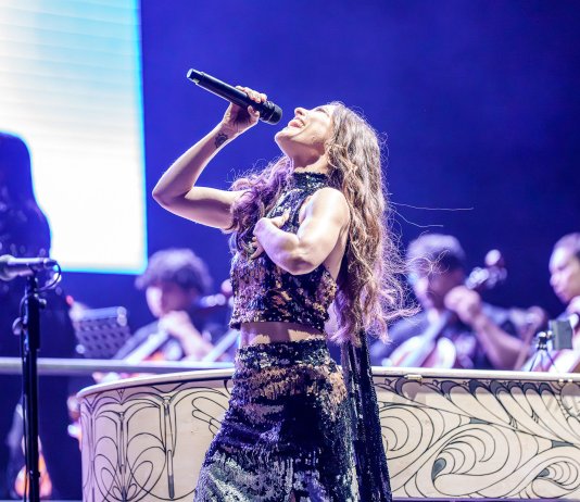 Por Maris Stella Fernández Brenes, Presidente Fundación SIFAIS Si alguien hubiera hecho, en frío, los números del concierto de nuestros 15 años antes de que ocurriera, probablemente habría recomendado no hacerlo. Solo el rubro de sonido, para un escenario de la envergadura de Parque Viva, no bajaba de 50 mil dólares. Necesitábamos una consola de mezcla de gran formato FOH capaz de recibir 500 líneas para integrar cientos de instrumentos, micrófonos y luces al mismo tiempo, lo que, de entrada, era algo fuera de serie para una fundación como la nuestra. que con costos tenemos un parlantito y un micrófono en nuestras instalaciones. Teníamos cuatro semanas de convocatoria formal y apenas dos ensayos generales para lograr que más de 230 personas —de edades, niveles y trayectorias musicales completamente distintas— sonaran como una sola orquesta capaz de acompañar a artistas de calidad internacional. Cualquier planificador de eventos, cualquier persona con una calculadora y sentido común, habría dicho que la ecuación no cerraba. Y no cerró, en efecto, varias veces. La víspera del concierto descubrimos que las 500 líneas no alcanzaban: se necesitaban 120 más. El presupuesto de sonido seguía siendo, sobre el papel, una cifra que no teníamos. No teníamos las pantallas gigantes usuales para estos eventos, y aunque las consiguiéramos, no había qué proyectar sobre ellas porque no teníamos expertos ni equipo en Circuito Cerrado de Televisión; no teníamos el transporte para trasladar a los 200 artistas (niños, jóvenes y adultos mayores) desde La Carpio, Birrí y San Diego hasta Parque Viva; no teníamos insumos para el “hospitality” acostumbrado detrás del escenario… Y aun así, uno por uno, cada obstáculo técnico se fue resolviendo hasta que, sumados todos, el resultado terminó siendo del todo desproporcionado con relación a lo que nosotros mismos habíamos previsto. ACME donó el sonido. Conseguimos las pantallas, los técnicos de circuito cerrado de televisión, los instrumentos faltantes, la exoneración del impuesto municipal por parte de la Municipalidad de Alajuela, veintitrés vallas de carretera donadas para difundir el proyecto, y la aprobación misma de Parque Viva para cedernos, de cortesía, uno de los escenarios más grandes y mejor equipados del país; Fotón nos cedió dos busetas para el transporte durante dos días; muchas empresas y personas donaron la alimentación.. Cada uno de esos puntos, por separado, habría sido motivo suficiente para que el concierto no se realizara. Juntos, bajo cualquier pronóstico técnico razonable, hacían que todo esto fuera increíble, inaudito, impensable. Y sin embargo se logró, y se logró con creces. Si a SIFAIS le hubieran cobrado absolutamente todo lo que ese concierto representó, la factura habría rondado los 395 mil dólares. A nosotros nos costó, en números reales, apenas 20 mil. Ninguna hoja de cálculo predice esa diferencia. Solo la explica algo que no cabe en una hoja de cálculo: la generosidad, sostenida y repetida, de decenas de personas y empresas que decidieron sumar. Ese mismo desafío al pronóstico razonable atraviesa, en realidad, toda la historia de SIFAIS, no solo este concierto. Cuando una vecina de La Carpio me planteó por primera vez la idea de crear una orquesta sinfónica en esa comunidad, hace quince años, a mí misma me sonaba a una locura tan grande como pensar en levantar un edificio de madera de cuatro pisos, con un sistema estructural totalmente inédito a nivel mundial, en un precario donde lo que faltaba, precisamente, era espacio. Y todo sin dinero y sin experiencia previa en nada de esto. La Cueva del Sapo en La Carpio era, para buena parte del país, un lugar temido incluso por sus propios vecinos, un barrio del que la gente prefería mantenerse lejos. En ese mismo espacio hoy se levanta Cuevadeluz, un Centro de Integración y Cultura. Ese cambio tampoco lo predijo ningún pronóstico técnico. El salto hasta Parque Viva nació también de una circunstancia adversa. En el concierto que hicimos en junio del año pasado en el Melico Salazar, las limitaciones propias del recinto no nos permitieron compartir del todo el mensaje de SIFAIS. En vez de resignarnos, la respuesta fue plantear una meta que en ese momento sonaba casi absurda: el año entrante lo hacemos en Parque Viva. Fue, literalmente, como decir “el año que viene vamos a la Luna”. Y catorce meses después, ahí estábamos. Ese mismo patrón se repite, historia tras historia, en las personas que hicieron posible esta noche. Pienso en Paola, que de niña jugaba con objetos que encontraba en un basurero y los convertía en juguetes, y que hoy es la primera mujer en haber hecho tramoya en el Teatro Nacional de Costa Rica. Pienso en Sara, que tuvo que reconstruir su vocación artística después de que la organización social donde trabajaba en su país tuviera que cerrar operaciones por el cierre de espacios para las ONG, y que hoy dirige a todo nuestro equipo de profesores de cuerdas. Pienso también en el violinista de 65 años que aunque no sabe leer ni escribir, decidió aprender a leer música, en los adultos mayores de Birri que llevan apenas año y medio tocando, en doña Alba, que participa cada semana en lo los distintos talleres trasladándose desde Tibas hasta la Carpio, o en los jóvenes que viajan desde otra provincia porque en la suya no encuentran un espacio así. Ninguna de esas historias estaba en el pronóstico. Todas terminaron sobre ese escenario. Jaime Gamboa, de Malpaís, lo resumió en una conversación durante los ensayos: dijo que sin duda allí en Cuevadeluz se evidencia que el arte transforma, que llega al corazón de la gente, y que puede ayudar a sacar adelante a un país entero. Yo agregaría que el arte, cuando se practica así, también es capaz de derrotar el cálculo. Porque en SIFAIS siempre hemos sostenido un principio muy simple: todos tienen acogida, sin importar su pasado, sus credos, su edad, su condición socioeconómica o su nacionalidad. Tenemos, entre nuestra gente, desde quien no sabe leer hasta quien tiene un doctorado de Oxford. Ese principio, que en el papel también podría sonar poco práctico, es precisamente lo que ha sostenido quince años de resultados que ningún pronóstico técnico habría anticipado. Al final, la matemática nunca cambió, ni cambiará. Los números seguían siendo los mismos, difíciles, ajustados, casi imposibles. Lo que cambia el resultado no fue una fórmula distinta, sino la insistencia de mucha gente en poner, una y otra vez, lo humano por encima de lo calculable. Esa es, para mí, la lección más honesta de estos 15 años de Sifais y de esta noche en particular: los pronósticos técnicos y matemáticos pueden decir que algo no es posible. El humanismo, cuando se sostiene con confianza, constancia, locura y ternura tiene la costumbre de demostrar que sí lo es.